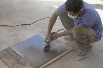 Worker cutting floor tiles with angle grinder at construction site