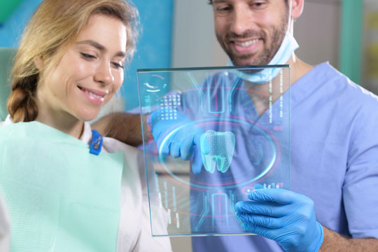 A futuristic dentist shows the futuristic holographic plate of the patient's dentition, and she smiles happily. Concept of: dentists, healthcare, medical examination, technology, future.