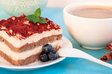 Italian tiramisu dessert on a porcelain plate, on a blue background