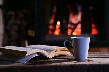 Cup of tea and a book on the table with fireplace in the blackground.