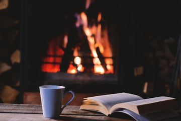 Cup of tea and a book on the table with fireplace in the blackground.