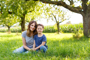 Fototapeta premium Beautiful young mother and little daughter sitting on green grass and resting