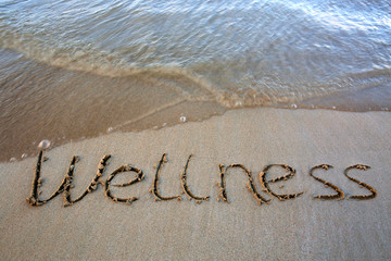 Fototapeta premium Word Wellness written on the sand near the sea.Vacation concept.