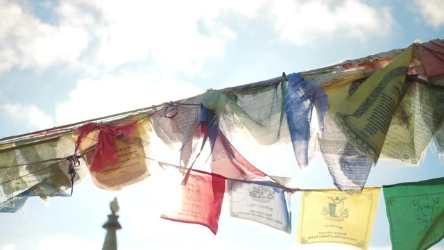 Buddhsit culture prayer flags flap in strong wind against sun flares, on top of high altitude mountain with sacred temple or base camp for climbers. Religion and blessing