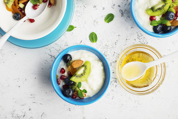 Breakfast, rice porridge or natural yoghurt with assorted berries, fruits and nuts: kiwi, pomegranate, blueberries, almonds, dried apricots in small bowls on a light background. Top view. Copy space.