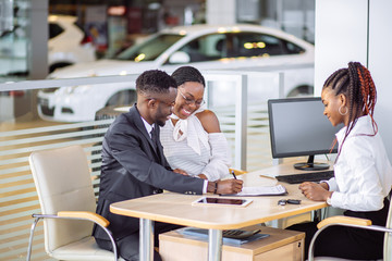 Smiling african couple buying new car at new car showroom