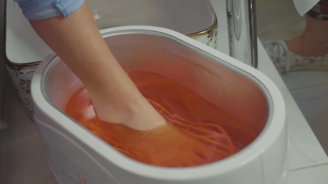 Wax bath for feet at beauty spa salon. Close-up in slow motion.