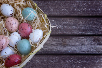 Multicolored easter eggs in a basket on a brown wooden table, Easter concept with space for text.