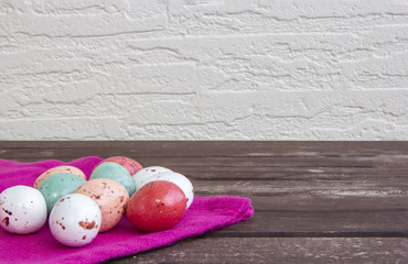 Colorful Easter eggs on a pink napkin / tablecloth on a brown wooden table and white wall.
