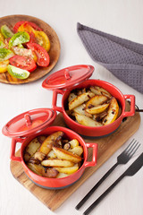 Two red pots of baked potatoes with onion and mushrooms. Home-made traditional recipe