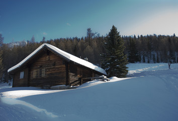 Fototapeta na wymiar small wooden mountain hut (cabin), old, covered by snow, high mountain, struck by a ray of sunshine, sunset, forest, isolated, fairytale, winter, Alps, Rothwald, Switzerland