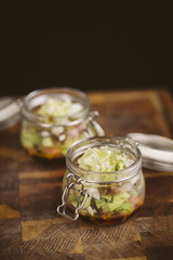Salmon tartare served in a glass jar on a wooden board. Black background.