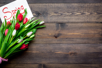 First spring flowers. Bouquet of colorful tulips near Spring lettering on dark wooden background top view copy space