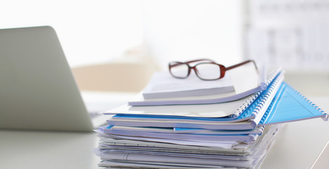 Laptop with stack of folders on table on white background