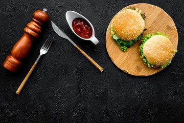 Burger on wooden cutting board on black background top view copy space