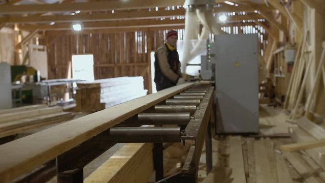 Caucasian woodworkers puts wood board on refiner machine at lumber-mill, floor covered in sawdust