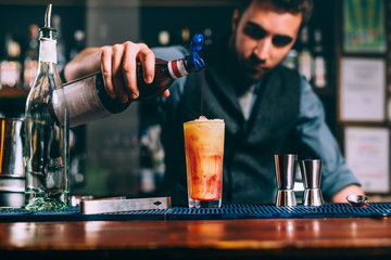 portrait of bartender pouring cherry syroup in orange summer cocktail. details of bar and restaurant