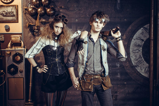 Young beautiful couple in suits in steampunk style wearing glasses and with guns.
