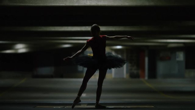 Young ballet dancer doing graceful poses under a car park light, in slow motion