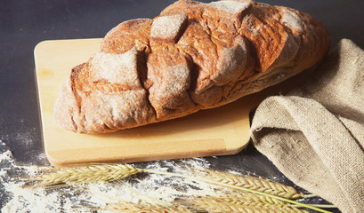 rustic crusty bread and wheat ears on a dark wooden table