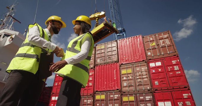 Businesswoman and dock worker shake hands at a busy shipyard. Shot on RED Epic.