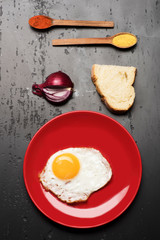 Dish with fried egg near spoons with spices, bread, onion