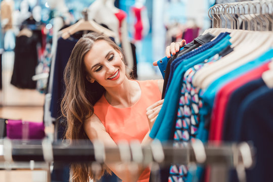 Frau sucht nach Kleid auf Kleiderstange im Mode Laden und sieht glücklich aus