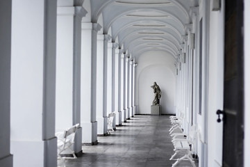 Female statue in the end of a bright hall alley with white walls