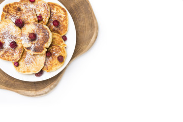 A plate of traditional russian cheesecakes lying on wooden board and decorated with strawberries. Top view on white background with copy space.