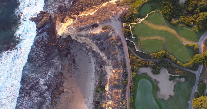 Aerial view from above of a coastal golf course with fairways and greens next to the ocean.