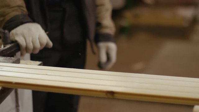 Workers pick up wood board running out carpenter jointer workbench at woodwork facility, lots of sawdust