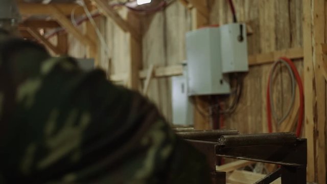 Caucasian woodworkers puts wood board on refiner machine at sawmill, floor covered in sawdust