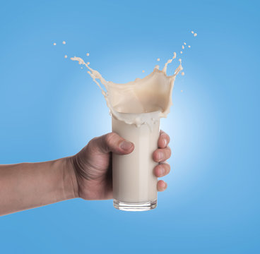 Hand holding glass of milk with a splash on a blue background
