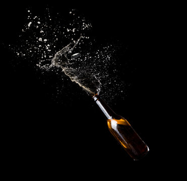 Gold beer bottle opening with exploding and splashing on dark background