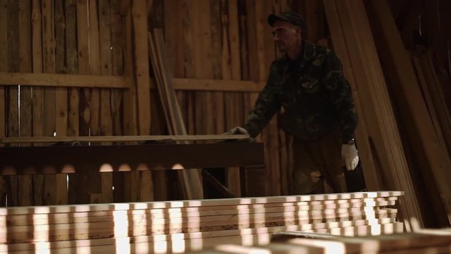 Caucasian carpenters puts board plank on refiner machine at sawmill, floor covered in sawdust