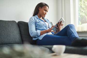 Young African woman sitting on her couch using a tablet