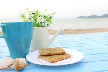 Top view of breakfast, blue cup of hot chocolate and cracker bread on white dish on blue wooden...