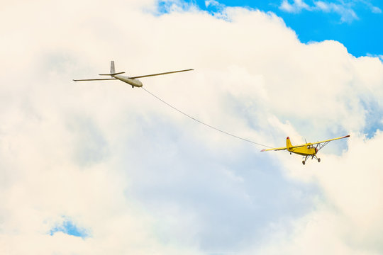 Yellow small light-engine sport plane flying in the cloudy sky pulls on a rope the glider plane