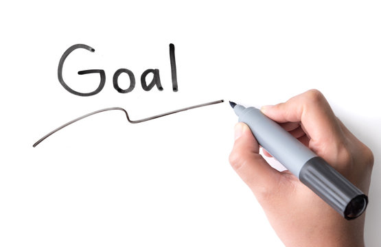 Hand holding black permanent marker and writing word "Goal"on white background