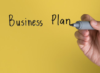 Hand holding black permanent marker and writing word "Business Plan"against yellow background © showcake