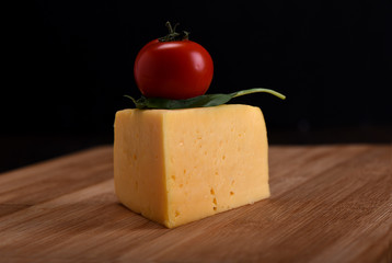 A piece of cheese with tomato and basil on a cutting board