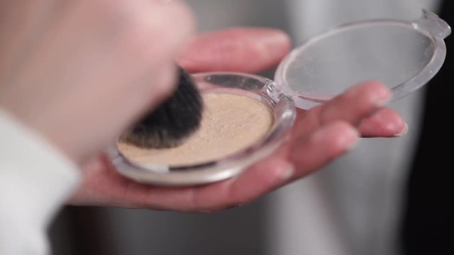 Close up shot of a make up artist getting powder on brush from a box. She is holding cosmetic powder.
