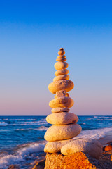 Fototapeta na wymiar Rock zen pyramid of white stones in the pink rays of the setting sun against the sea