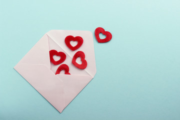 White envelope with red hearts on blue paper or cardboard background.