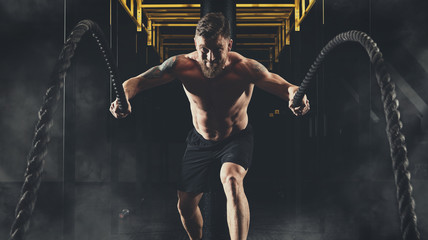 Man working out with battle ropes at gym