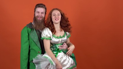 Young couple in costumes celebrating saint patrick's day isolated on orange wall hugging