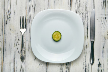Eating for a girl, women on a strict diet. Two little funny green cucumber with pimples on a white plain plate. Too little food for losing weight. Anti-obesity diet by evil nutritionist.