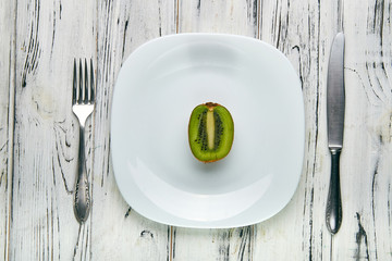 Eating for a girl, women on a strict diet. Half a juicy sweet ripe green kiwi on a white plain plate. Too little food for losing weight. Anti-obesity diet by evil nutritionist.