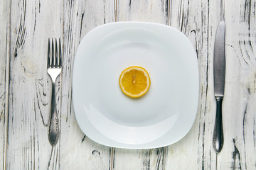 Eating for a girl, women on a strict diet. Bright yellow sour lemon on a white plain plate. Too little food for losing weight. Anti-obesity diet by evil nutritionist.