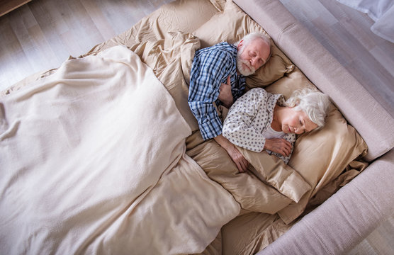 Sweet dreams. Top view of calm elderly husband and wife lying in bedroom. Their eyes are closed. Pensioners are relaxing in bed and hugging